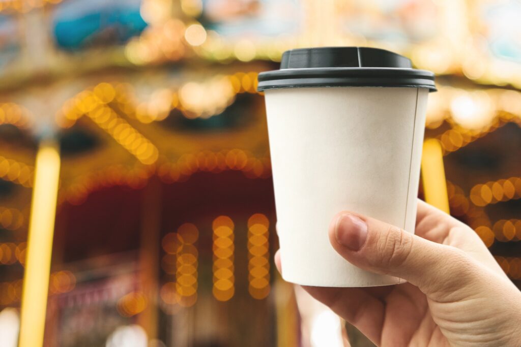 Someone holding disposable catering supplies in form, of white paper cup with black plastic lid.